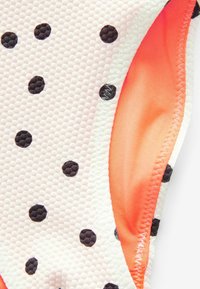 Costume da bagno rosa chiaro con tessuto testurizzato e pois neri. L'interno ha una foderatura arancione, che presenta colori contrastanti.