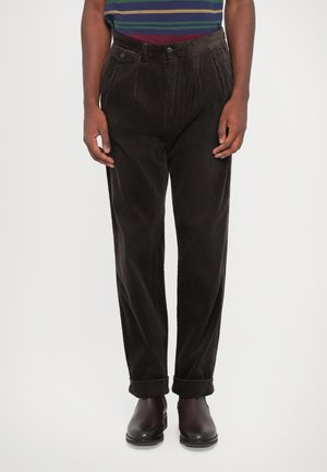 Brown corduroy pants with a straight leg design, featuring front pleats, side pockets, and rolled cuffs, paired with dark shoes.