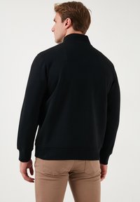 Black sweatshirt with a high collar, long sleeves, and a relaxed fit. Smooth fabric texture, minimalistic design with no visible logos.