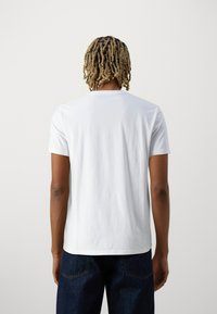 T-shirt en coton blanc avec un col rond, des manches courtes et une coupe décontractée. Sans motifs ni graphiques, texture lisse. Vue de dos montrée.