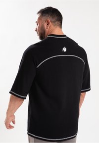 Zwarte korte mouwen shirt van textuurstof, met grijze accentstiksels en een klein logo op de achterkant nabij de halslijn.