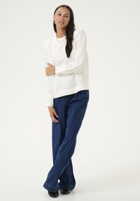Witte blouse met lange mouwen, een gladde textuur en manchet, gecombineerd met losse donkerblauwe spijkerbroeken. Eenvoudige lijn, minimale styling.