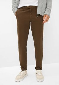 Chinos marron en matériau léger, dotés d'une fermeture à bouton et de poches latérales, associés à des baskets blanches.