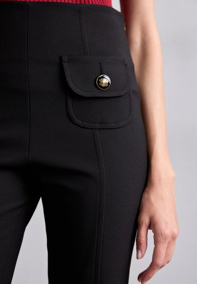 Svarta skräddarsydda byxor med en klaffficka prydd med en guldkknapp. Slät tyg, slim fit och ren sömnad längs sömmarna.