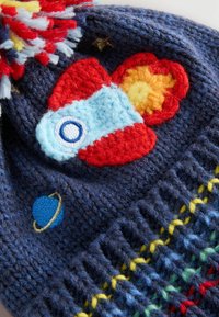 Bonnet tricoté bleu marine avec des motifs colorés de fusée et de planète brodés. Il est doté d'un pompon multicolore et d'un détail côtelé texturé.