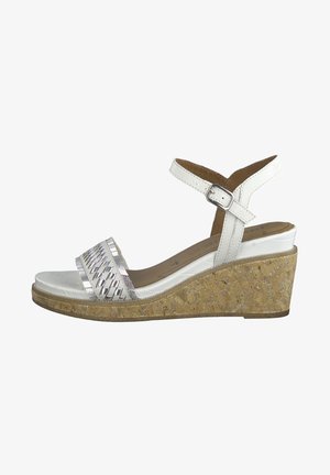 Sandale blanche à talon compensé avec semelle en liège, bride tissée métallisée sur les orteils, et sangle de cheville réglable.