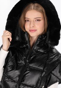 Czarna kurtka puchowa o połyskującym wykończeniu, pikowanym wzorze i kapturze z futerkiem. Zapinana na zamek błyskawiczny, z widocznymi przeszyciami podkreślającymi strukturę.