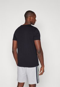 Μαύρη κοντομάνικη μπλούζα με στρογγυλή λαιμόκοψη, σε συνδυασμό με ανοιχτό γκρι σορτσάκι που έχει πράσινες και μπλε πλευρικές ρίγες. Λείος υφασμάτινος σύνθεση.