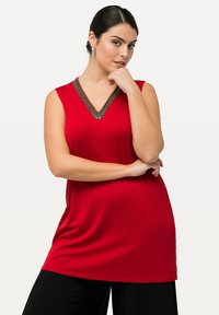 Červená bezramenní tunika s výstřihem do V, zdobená dekorativními korálky. Měkká látka, volný střih a padá pod boky. Černé široké kalhoty.