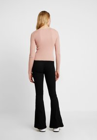 Pull côtelé rose clair à manches longues, coupe ajustée, col arrondi, associé à un pantalon noir évasé et des chaussures blanches.