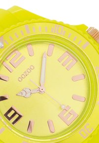 Montre en silicone jaune vif avec un cadran rond, des index horaires roses et des aiguilles. Dispose d'un affichage de la date à la position de 6 heures.