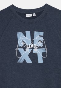 Sudadera color azul marino con un gráfico de un controlador de videojuegos y las palabras "NEXT LEVEL" en azul claro. Tejido suave con un cuello acanalado.