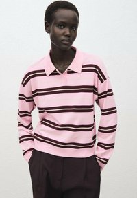 Rosa- und braun gestreifte Langarm-Polohemd mit Kragen, das einen lässigen Schnitt und gerippte Bündchen aufweist. Dunkle Hosen ergänzen das Outfit.