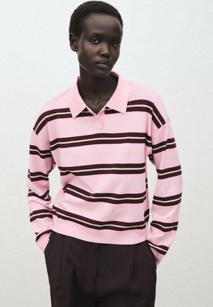 Polo à manches longues rayé rose et marron avec un col, présentant une coupe décontractée et des poignets côtelés. Un pantalon sombre complète la tenue.