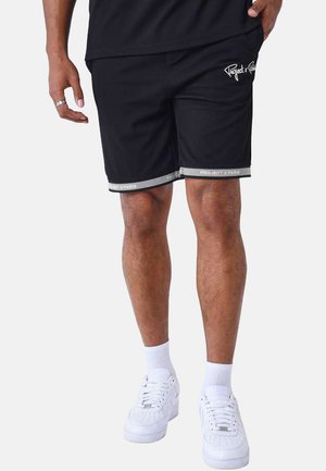Shorts de sport noirs avec logo blanc, ceinture élastique et accents rayés réfléchissants à l'ourlet. Portés avec des baskets blanches et des chaussettes à la cheville.
