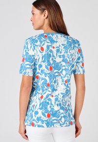 Camiseta de manga corta azul con un patrón floral multicolor que presenta acentos en rojo y blanco; fabricada con una tela suave y con un cuello redondo.