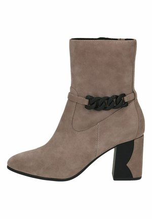 Botte de cheville en suède beige avec un talon bloc, ornée d'une chaîne noire autour de la cheville et d'un design à bout pointu. Texture lisse.