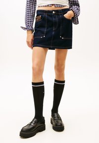 Tumesinises toonis teksaseelik heledate õmblustega, ees taskud ja pruun detail. Sobitatud mustade põlvikute ja paksu tallaga mokassiinidega.