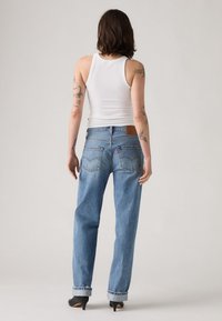 Lichtblauwe denim jeans met een relaxte pasvorm, opgerolde mouwen en een bruine leren patch op de achterkant van de tailleband. Gecombineerd met een witte tanktop.
