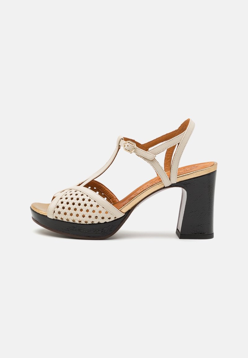 Sandale beige à bout ouvert avec devant tissé, bride de cheville avec boucle, semelle intérieure rembourrée beige, talon carré noir, et bordure dorée sur le bord de la semelle.