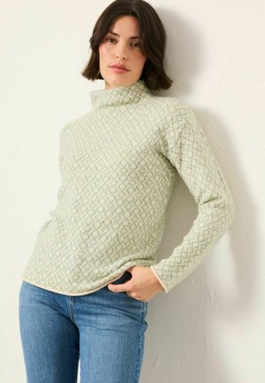 Light green turtleneck sweater with a diamond pattern, soft texture, long sleeves, and a cream-colored hem. Worn with blue jeans.
