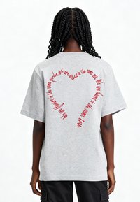Szary, oversize'owy t-shirt z krótkimi rękawami. Na plecach znajduje się czerwona, kursywna napisana tekst w kształcie serca. Miękka, przypominająca bawełnę tekstura.