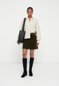 Lysternet ternet button-up skjorte med puffede ærmer, olivengrøn corduroy nederdel, sorte knæ-høje støvler og en struktureret sort taske.