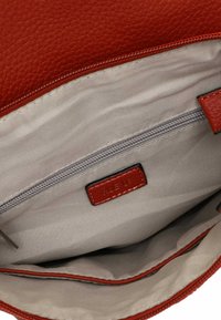 Rotes texturiertes Lederhandtascheninnere mit einem hellen Stofffutter, das eine Reißverschlusstasche und ein gesticktes Etikett zeigt.