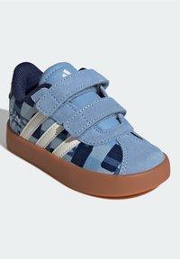 Chaussure en toile bleue avec des sangles à Velcro, présentant un motif aux nuances de bleu, des rayures blanches, et une semelle en caoutchouc marron.