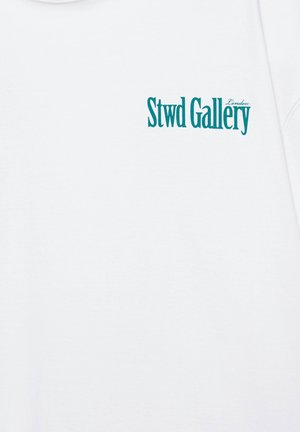 Vêtement blanc avec texte bleu sarcelle "Stwd Gallery" et un plus petit "London" imprimés en haut à gauche.
