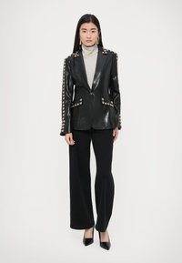 Crni kožni blejzer sa zlatnim ukrasnim gumbima, reverima s usjekom i prilagođenim krojem, uparen s sivim rolkom i širokim hlačama.