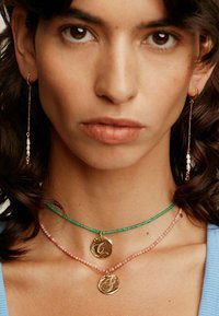 Collares de colgante de oro con grabados de iniciales, uno en una cadena de cuentas verdes, el otro en una cadena de cuentas rosas; acompañados de largos pendientes de perlas.