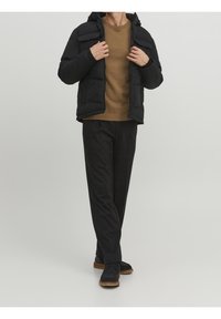 Black puffer jacket with a hood, zip closure, and quilted design, paired with a brown sweater and black trousers. Footwear features a textured sole.