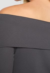 Grå av-axel topp med ribbad struktur. Har en bred halsringning som sitter löst och är elastisk för en kroppsnära silhuett.