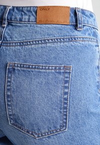 Světle modré džínové kalhoty s kapsou na zadní části a hnědým koženým štítkem s nápisem "ONLY." Vyznačují se viditelným švem a hladkým povrchem.