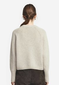 Ljusgrå stickad tröja med en bred rund halsringning, ribbade ärmslut och en kortad nederkant. Har ett mjukt, strukturerat tyg och raglanärmar.