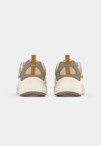 Des baskets beige et vert olive avec un panneau en maille texturé, une semelle blanche et un accent orange à l'arrière. Forme arrondie et design rembourré.