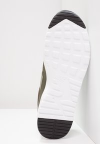 Nike tenisky s převážně olivovým svrškem, bílou gumovou podrážkou, texturovanou černou patou a vzorovaným dezénem na podešvi.