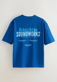 Tricou albastru cu mânecă scurtă, cu textul "Hickory Hollow SOUNDWORKS din Franklin și Knoxville, mixare & masterizare din 1957" pe spate.