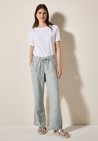 Lichtgrijs en witte gestreepte broek met een elastische tailleband en trekkoord, gecombineerd met een eenvoudig wit T-shirt met korte mouwen en sandalen.