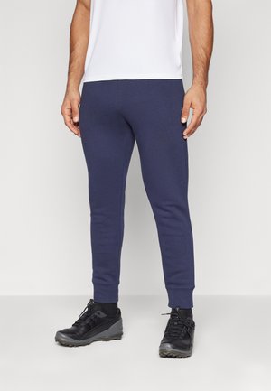 Marineblaue Jogginghosen mit slim-fit Design, elastischem Bund und gerippten Knöchelbündchen, kombiniert mit schwarzen Sportschuhen.