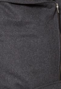 Dunkelgrauer Stoff mit einer weichen, strukturierten Oberfläche. Verfügt über einen Reißverschluss, der durch einen glatten, metallischen Reißverschluss an der Seite hervorgehoben wird.