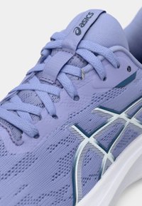 Πορτοκαλί αθλητικό παπούτσι με υφασμάτινη επάνω επιφάνεια, επίπεδα κορδόνια, και αντιθέσεις σε μπλε και λευκό χρώμα. Διαθέτει λογότυπο στη γλώσσα και στο πλάι.