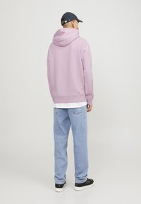 Sudadera rosa claro con una gran capucha, puños y dobladillo acanalados; llevada sobre una camiseta blanca. Combinada con jeans azul claro y zapatillas negras.