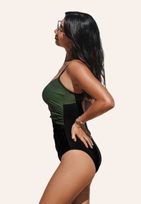 Maillot de bain une pièce en vert foncé et noir. Il présente des bretelles fines, un devant texturé et un tissu lisse. La vue de côté met en avant les lignes de conception.
