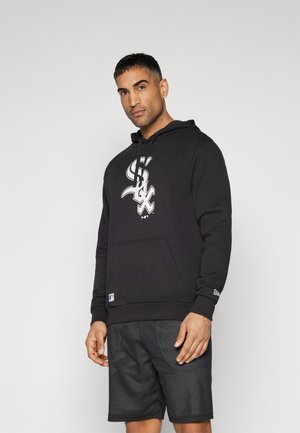 Sudadera negra con capucha y bolsillo frontal, adornada con un logo blanco. Combinada con pantalones cortos de malla negra con textura perforada.