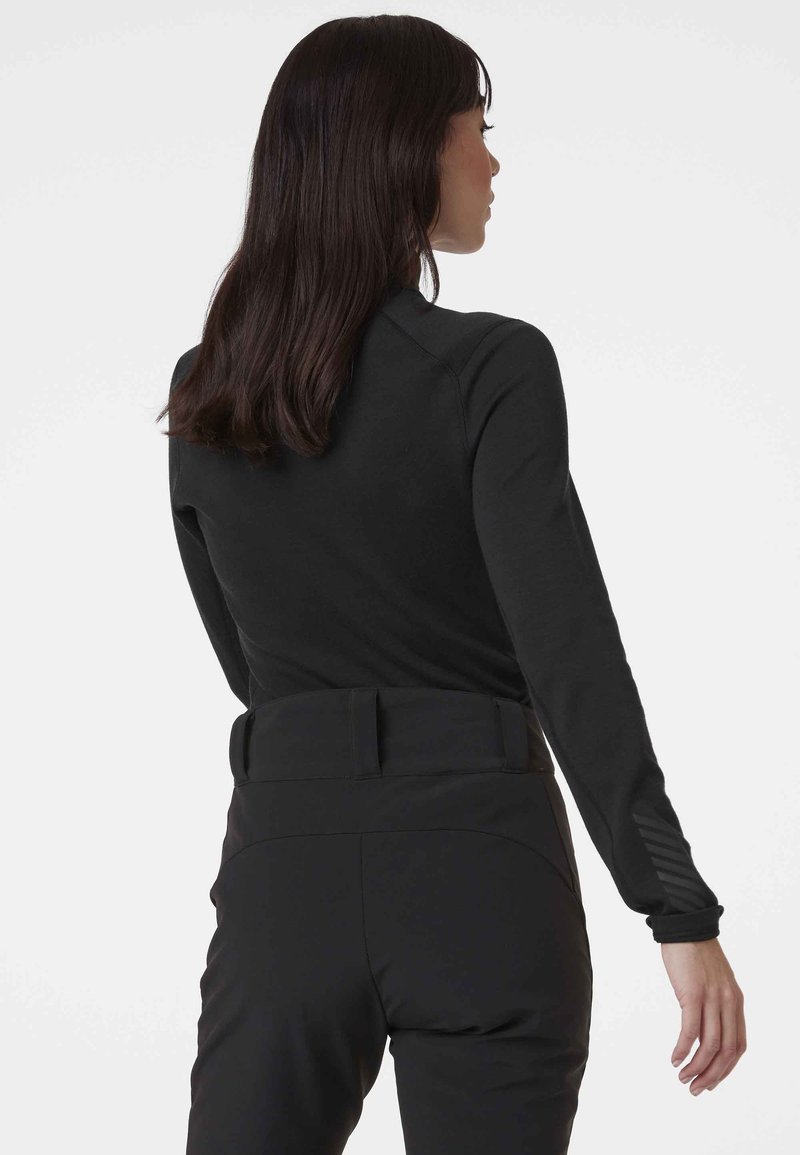 Top negro de manga larga con un diseño ajustado, que presenta una textura suave y puños acentuados, combinado con pantalones negros de cintura alta.