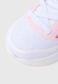 Primo piano della punta di una scarpa da sport bianca e rosa con tessuto a rete traspirante e lacci bianchi su sfondo chiaro.