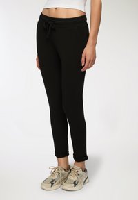 Czarne spodnie dresowe w dopasowanym kroju z elastycznym paskiem w talii i sznurkiem do regulacji. Posiadają boczne kieszenie i mankiety przy kostkach. W komplecie z beżowymi trampkami.
