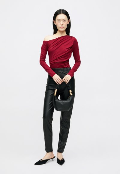 Camisola burgundy ombro a ombro com design drapeado, combinada com calças pretas em pele sintética. Mala preta com ferragens douradas e saltos pretos pontiagudos.